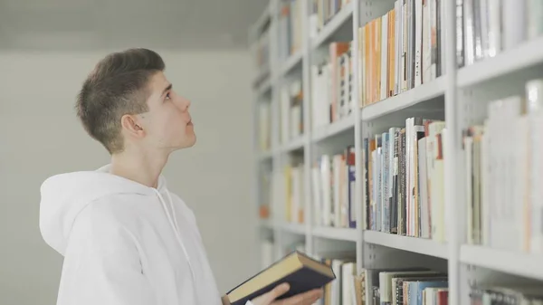 Человек ищет книгу на книжных полках в библиотеке в колледже — стоковое фото