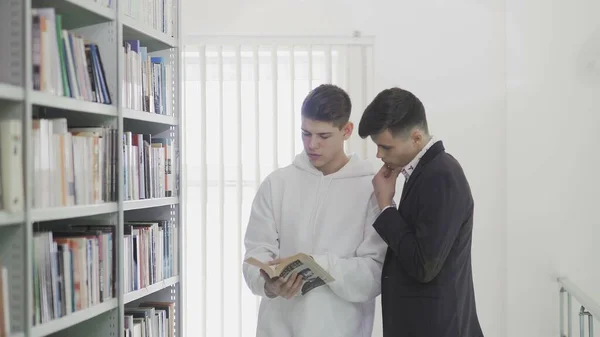 Два друга студентов ищут книгу на книжных полках в библиотеке в колледже — стоковое фото