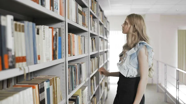 Blonde student woman taking book from shelf in university library. — Stock Photo, Image