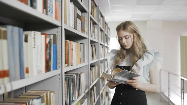 Blonde student woman taking book from shelf in university library.