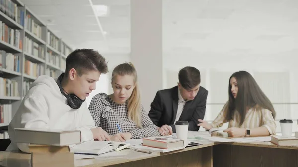 College students working together preparing for exams while sitting at table at university library — Stock Photo, Image