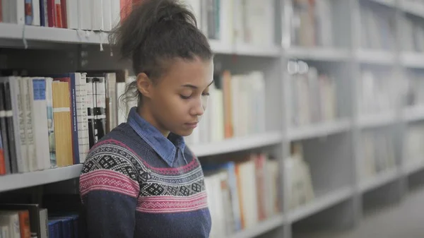 Young african american woman is reading book sitting on floor in university library. — Stock Photo, Image