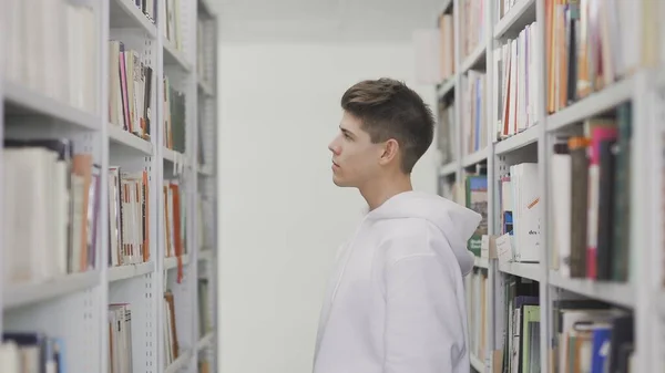 Молодой студент ищет книгу с книжной полки в библиотеке — стоковое фото