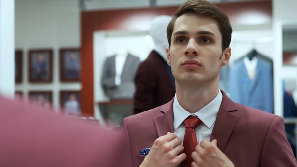 Man is looking at the mirror and wearing a red jacket at boutique — Stock Photo, Image