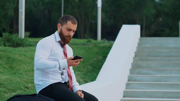 Empresário atraente olhando para um telefone celular, sentindo-se feliz e saindo — Fotografia de Stock