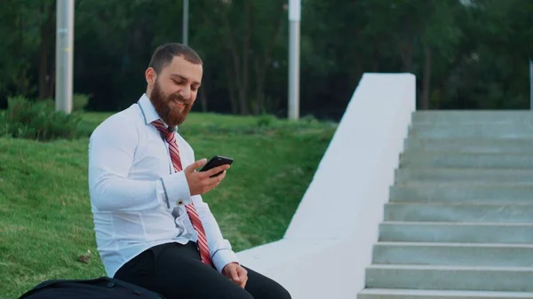 Empresário atraente olhando para um telefone celular, sentindo-se feliz e saindo — Fotografia de Stock