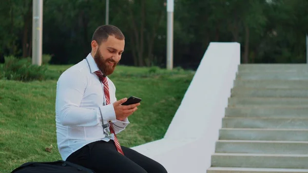 Empresário atraente olhando para um telefone celular, sentindo-se feliz e saindo — Fotografia de Stock