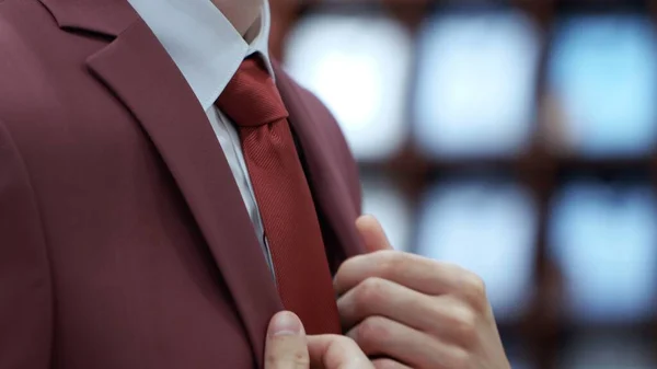 Side View of Young Business Man Fixing his Tie and red jacket Stock Photo