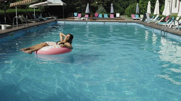 La donna galleggia con un cerchio di ciambelle gonfiabili nella piscina rigogliosa — Foto Stock