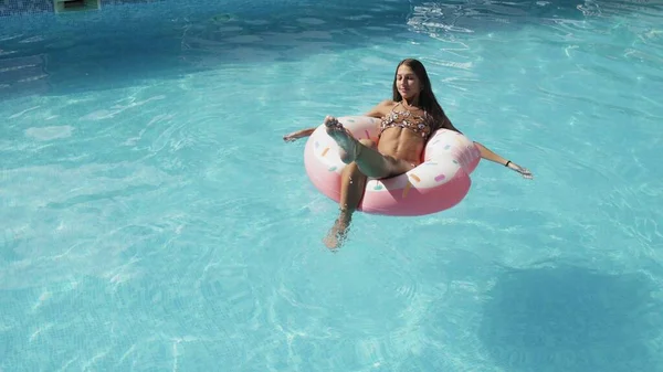 Una joven pasa tiempo en la piscina, toma el sol en un círculo inflable y nada en el agua — Foto de Stock