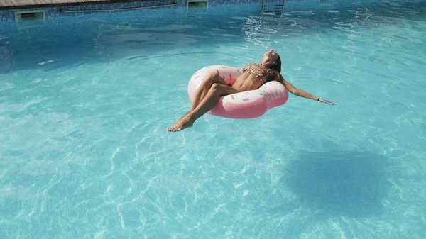 En ung flicka tillbringar tid i poolen, hon solar på en uppblåsbar cirkel och simmar i vattnet — Stockfoto
