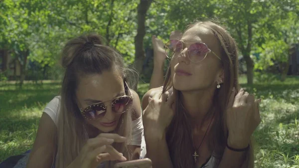 Duas belas mulheres jovens em óculos de sol são mentira na grama verde — Fotografia de Stock