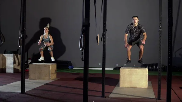 Athletic man and woman does set of box jumps at a crossfit gym — Stock Photo, Image