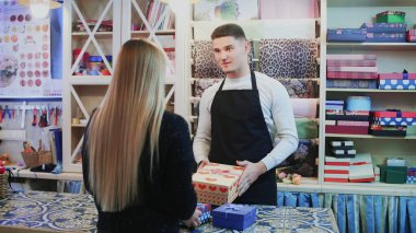 Çiçekçi adam hediye kutusunu müşteriye satar.