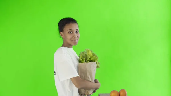 Wanita yang bahagia mengisi kantong kertas dengan sayuran dan buah-buahan yang sehat organik pada latar belakang kunci kroma — Stok Foto