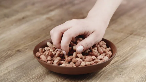 Woman Picks Up a handful of peanuts, To Eat, From Her Bowl. took a nut on the left side