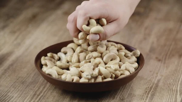 Woman Picks Up A handful Cashew, To Eat, From Her Bowl. took a nut on the right side