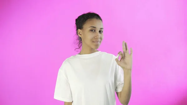 CuteAfro-American Girl toont ok met twee duimen en glimlachen op roze achtergrond in Studio — Stockfoto
