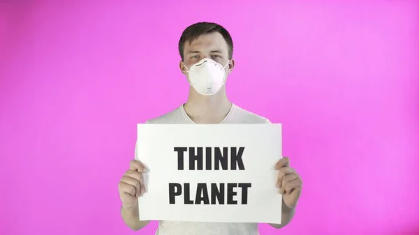 Молодой человек-активист с маской на лице и с постером Think Planet на розовом фоне — стоковое фото