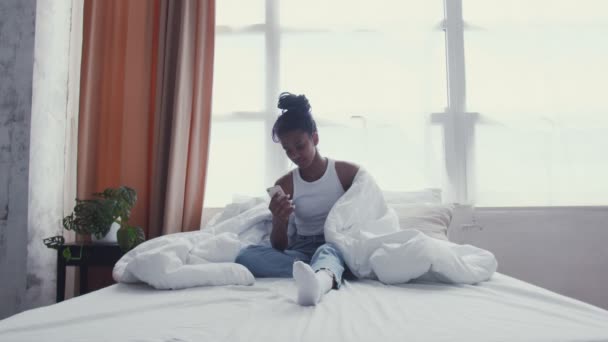 Pretty Young African American Woman χρησιμοποιεί το τηλέφωνο, ενώ χαλαρώνοντας στο κρεβάτι — Αρχείο Βίντεο