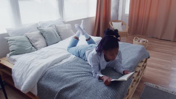 Attrayant jeune femme afro-américaine se couche dans son lit et lit le livre — Video