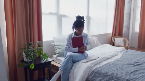 若いアフリカ系アメリカ人の女性がベッドに座って絵を描く — ストック動画