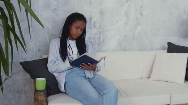 Привлекательная занятая африканская женщина сидит на стуле и делает заметки в своей записной книжке — стоковое видео