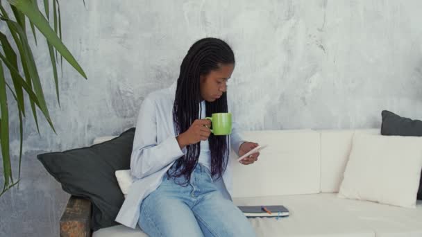 Femme africaine joyeuse boit du café et utilise un téléphone intelligent — Video