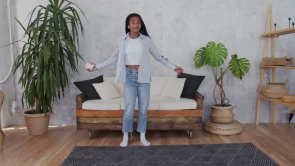 Щаслива молода чорна жінка з навушниками танцює в кімнаті . — стокове відео