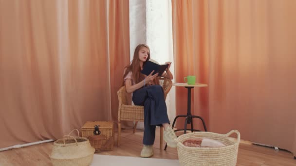 Jonge vrouw die boek leest in gezellige woonkamer, pagina omslaat, leren, studeren, onderwijs, boeken lezen, glimlachen — Stockvideo