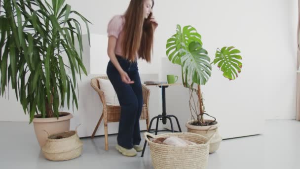 Mulher bonita lendo um livro em sua sala de estar em casa. Relaxado jovem mulher sentado perto de plantas da casa — Vídeo de Stock