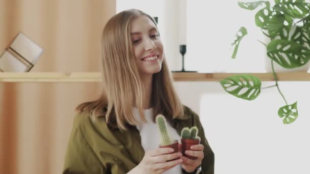 Ung kvinnlig trädgårdsmästare ler och poserar framför kameran med sina små favoritkaktusar i händerna. — Stockvideo