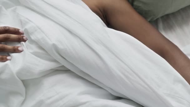 Молодая африканка просыпается в постели в своей спальне. Привлекательная женщина лежит на белом простыне — стоковое видео