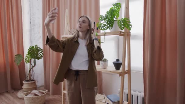Ung kvinna tar selfie med sina krukväxter på hyllan — Stockvideo