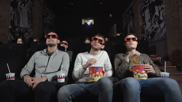 Trois amis avec des lunettes 3D regardent un film et mangent du pop-corn — Photo