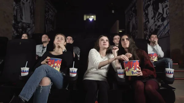Three pretty female friends are watching a scary movie.Middle woman reacts with shock.