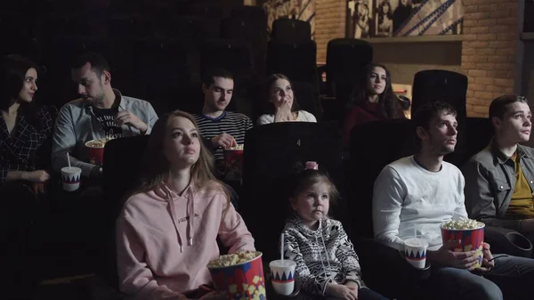 Young people sitting at the cinema, watching a film and eating popcorn, friendship and entertainment concept Stock Photo