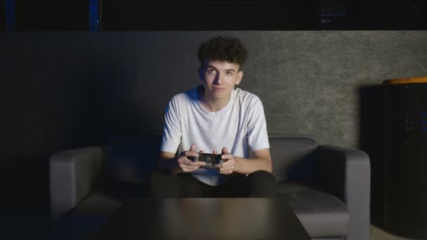 Забавно збуджений молодий чоловік переможець геймера тримає джойстик контролер, граючи у відеоігри, сидячи на дивані, відчуваючи себе задоволеним святкуванням перемоги у відеогрі вдома — стокове відео