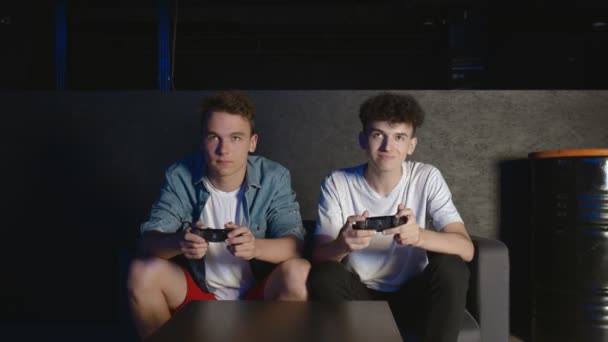 Två unga vänner spelar actionspel i vardagsrummet sittandes i soffan. En av dem slutade spela, tog farväl och stack. — Stockvideo