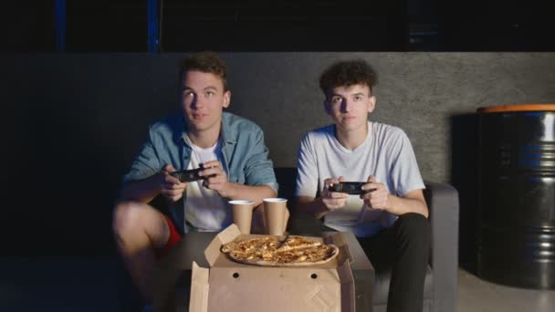 Dans le salon Deux amis assis sur un canapé Jouer au jeu vidéo et manger de la pizza. — Video