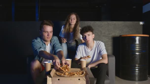 Jóvenes amigos terminaron de jugar a la consola de juegos y comenzaron a comer pizza en la habitación oscura. — Vídeo de stock