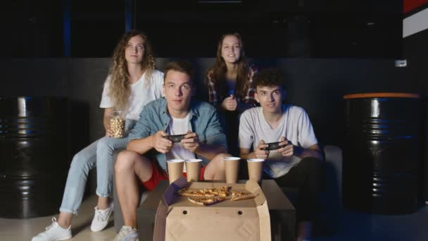 Young friends playing on the game console. Two men holds controllers and plays while girlfriends watches — Stock Video