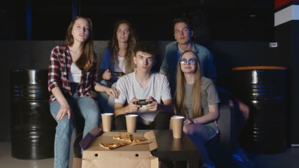 Feliz grupo de amigos jugando videojuegos en casa. Hombre y mujer están jugando mientras sus amigos sugieren — Vídeos de Stock