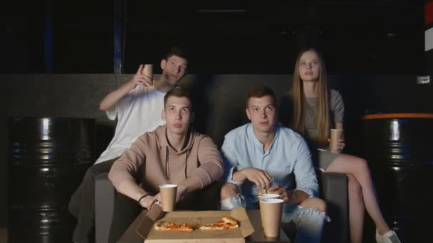 Grupo de jóvenes amigos viendo televisión juntos en el sofá, comunicándose, comiendo palomitas de maíz y pizza — Vídeo de stock