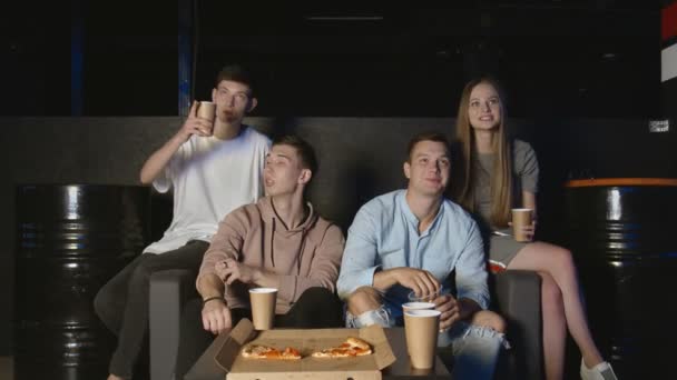 Group of young friends watching football together on couch, communicating, eating popcorn and pizza — Stock Video