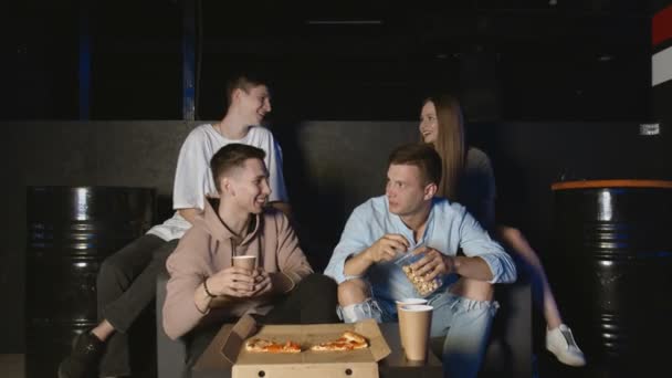 Портрет молодых друзей, которые едят попкорн во время просмотра спортивной игры по телевизору и говорят о действиях игроков — стоковое видео