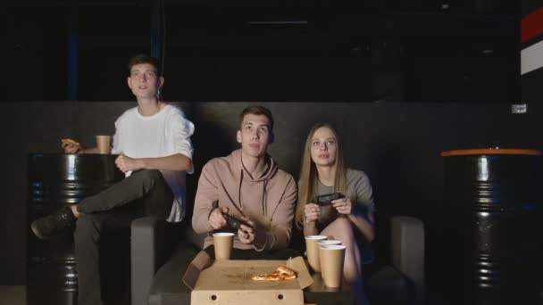 Bir grup konsantre arkadaş konsol oyununda oynuyor, kadın erkeğe karşı. Pizza yiyor. — Stok video