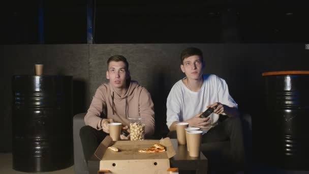 Два друга наслаждаются отдыхом на диване, играя в видеоигры — стоковое видео
