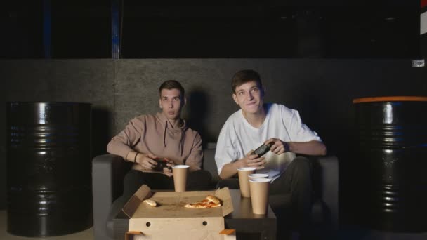 Два красивых молодых парня играют в видеоигры и едят пиццу. — стоковое видео