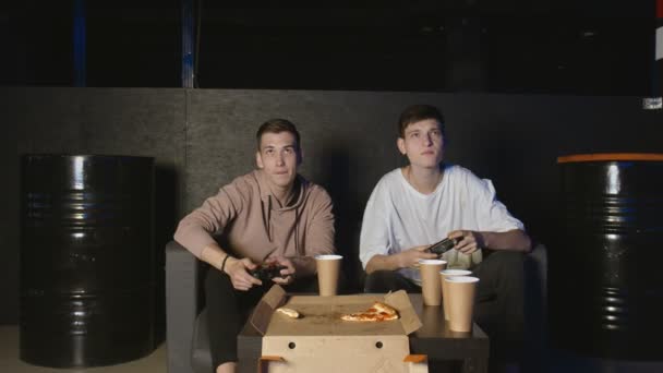 Deux amis heureux jouant à un jeu vidéo d'action dans le salon assis sur le canapé. Une compétition intense entre deux jeunes joueurs masculins est pleine d'émotions. — Video